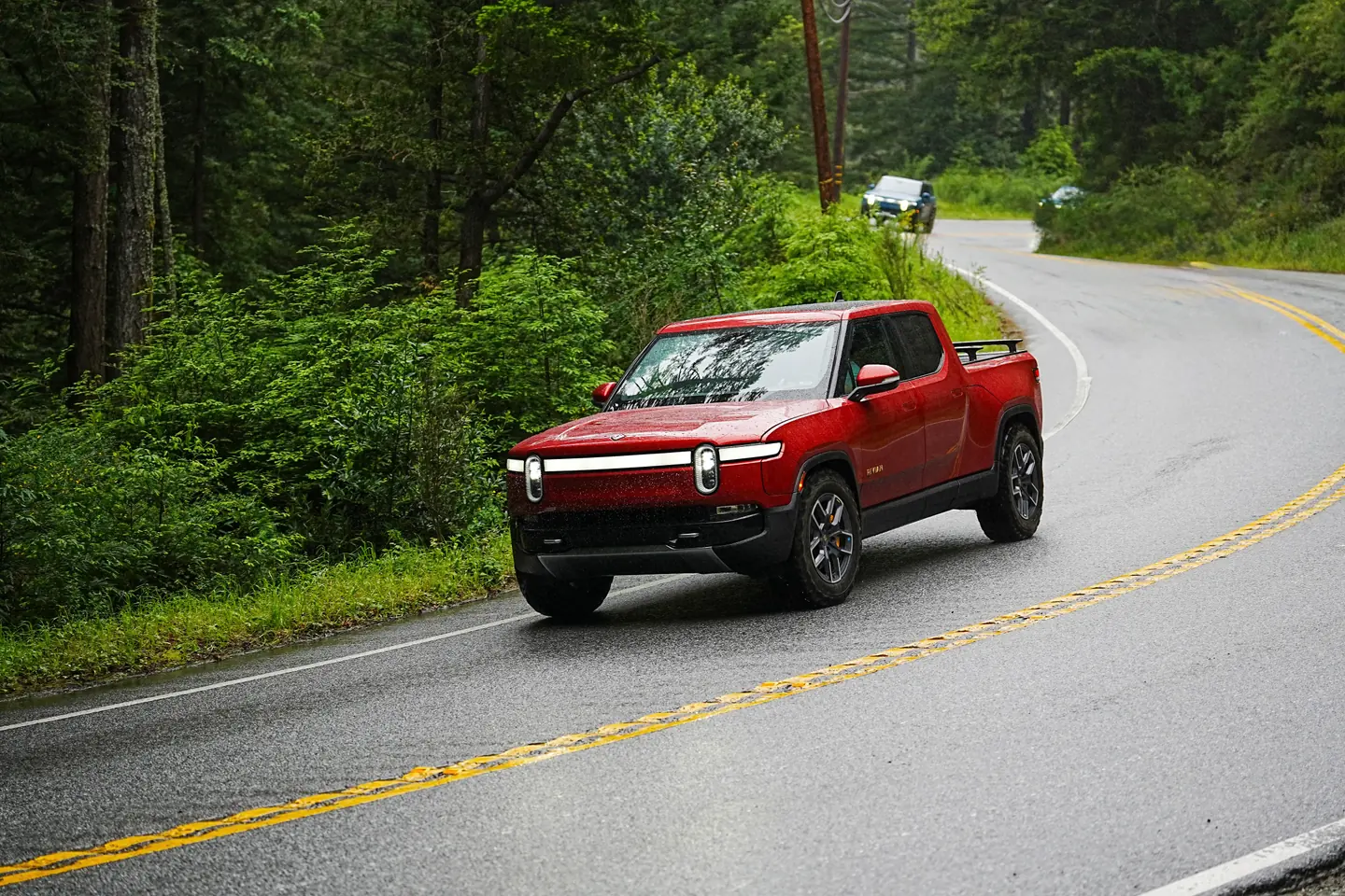 A red Rivian R1T rounding a wet forest road